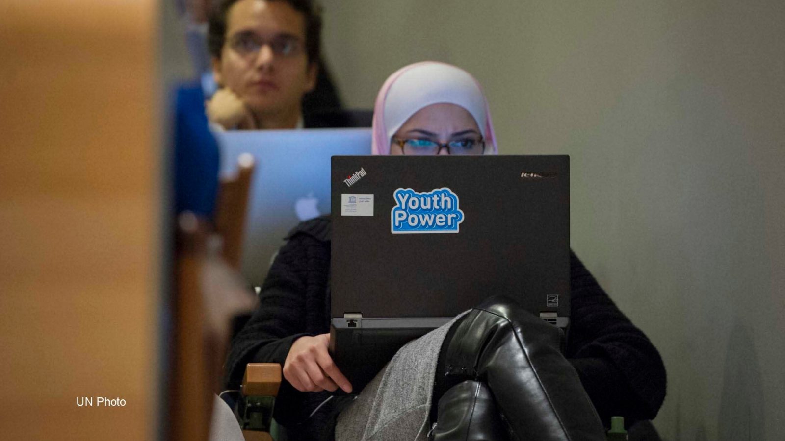 a girl at a UN meeting with a laptop sticker that says 'youth power'