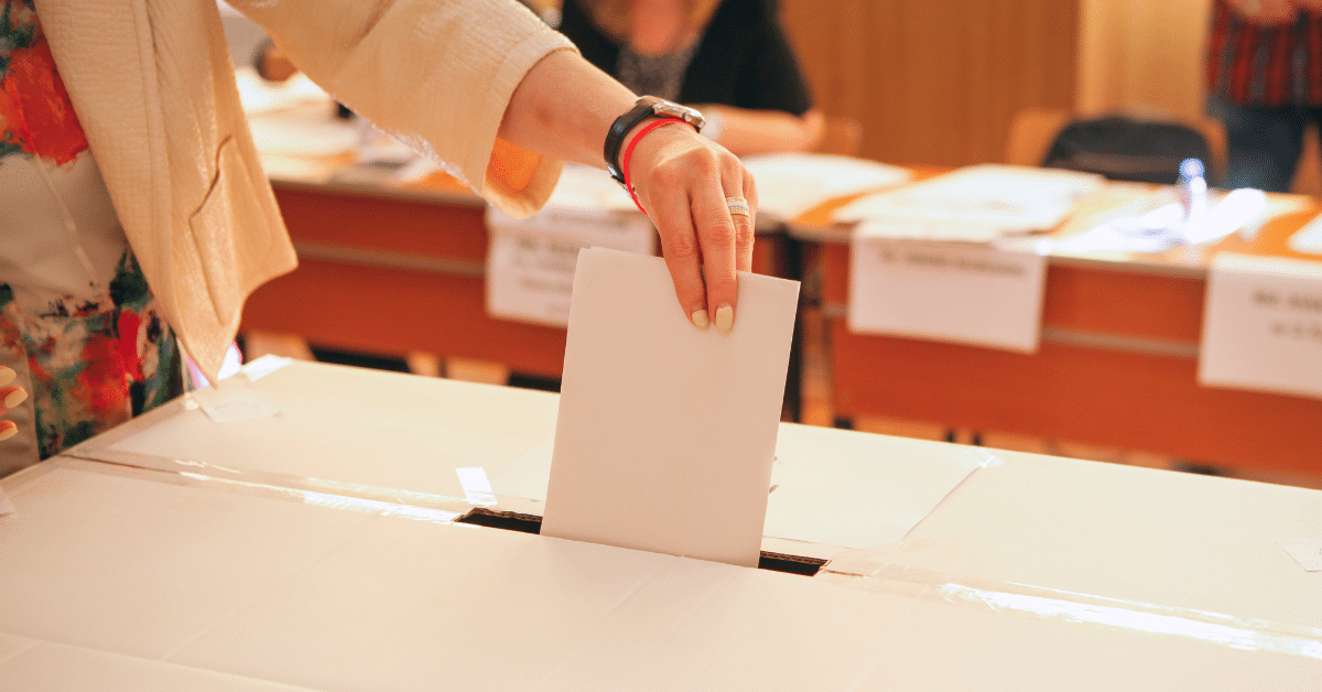 A photo of a white woman putting a vote into a voting box.