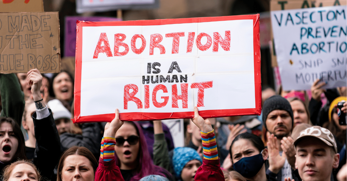 A pro-abortion protest. There is a large crowd, and a young person with blue hair in the centre of the crowd holds a sign that says "Abortion is a human right" in red and black letters.
